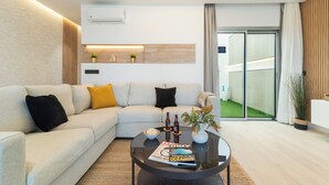 A modern living room with a sofa, coffee table, and a magazine. There is a wooden shelf with plants and a wall-mounted air conditioner.