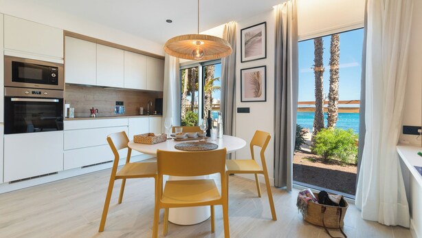 A modern kitchen with white cabinets, a built-in oven, and a dining area with a round table and chairs.