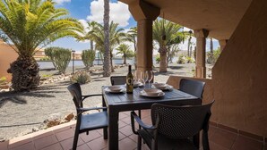 Een buitenterras met een tafel gedekt voor twee personen, omringd door stoelen, palmbomen en uitzicht op een waterpartij.