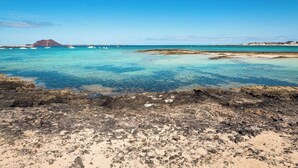 Een rotsachtige kustlijn met helder turquoise water en boten in de verte.