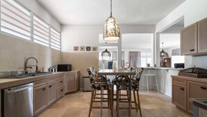 A modern kitchen with a central island, bar stools, and a hanging light fixture.