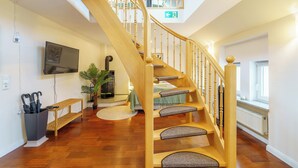 A spacious room with a wooden staircase, a flat-screen TV mounted on the wall, a potted plant, and a bench. - Residenz am Hostentor (Lübeck)