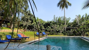 Una piscina con agua azul cristalina, rodeada de palmeras y sillas de descanso azules.