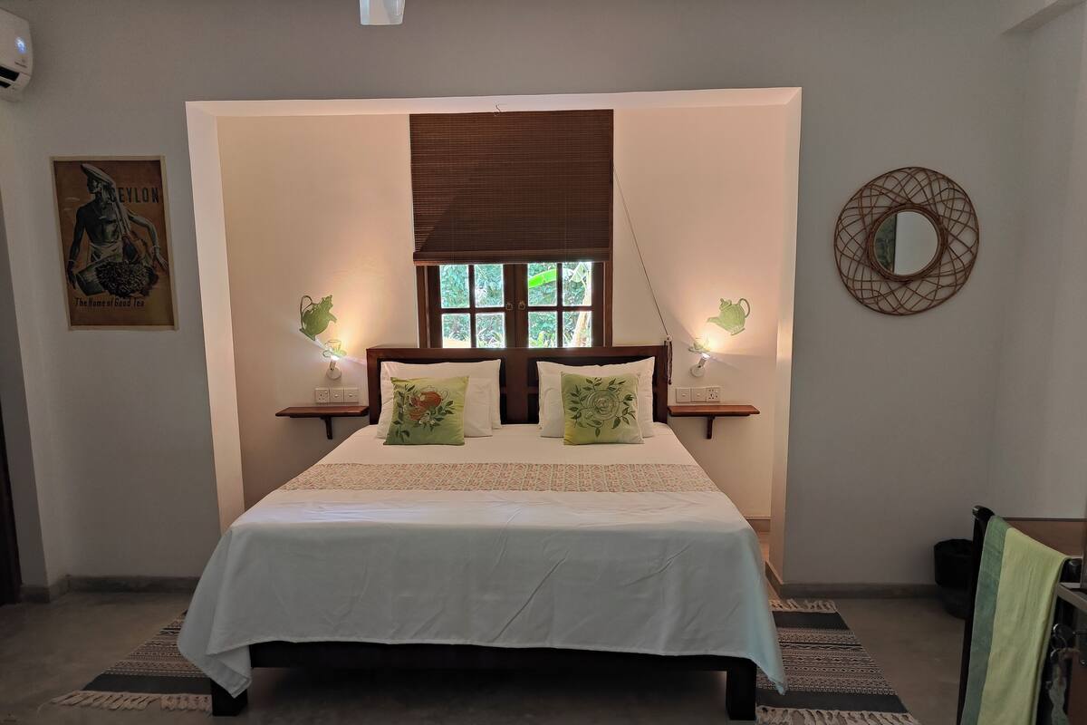 Un dormitorio ordenado con una cama grande, dos mesitas de noche con lámparas, una ventana con persianas y un espejo montado en la pared.
