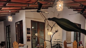 Un comedor con mesas y sillas de madera, un árbol decorativo e iluminación colgante.