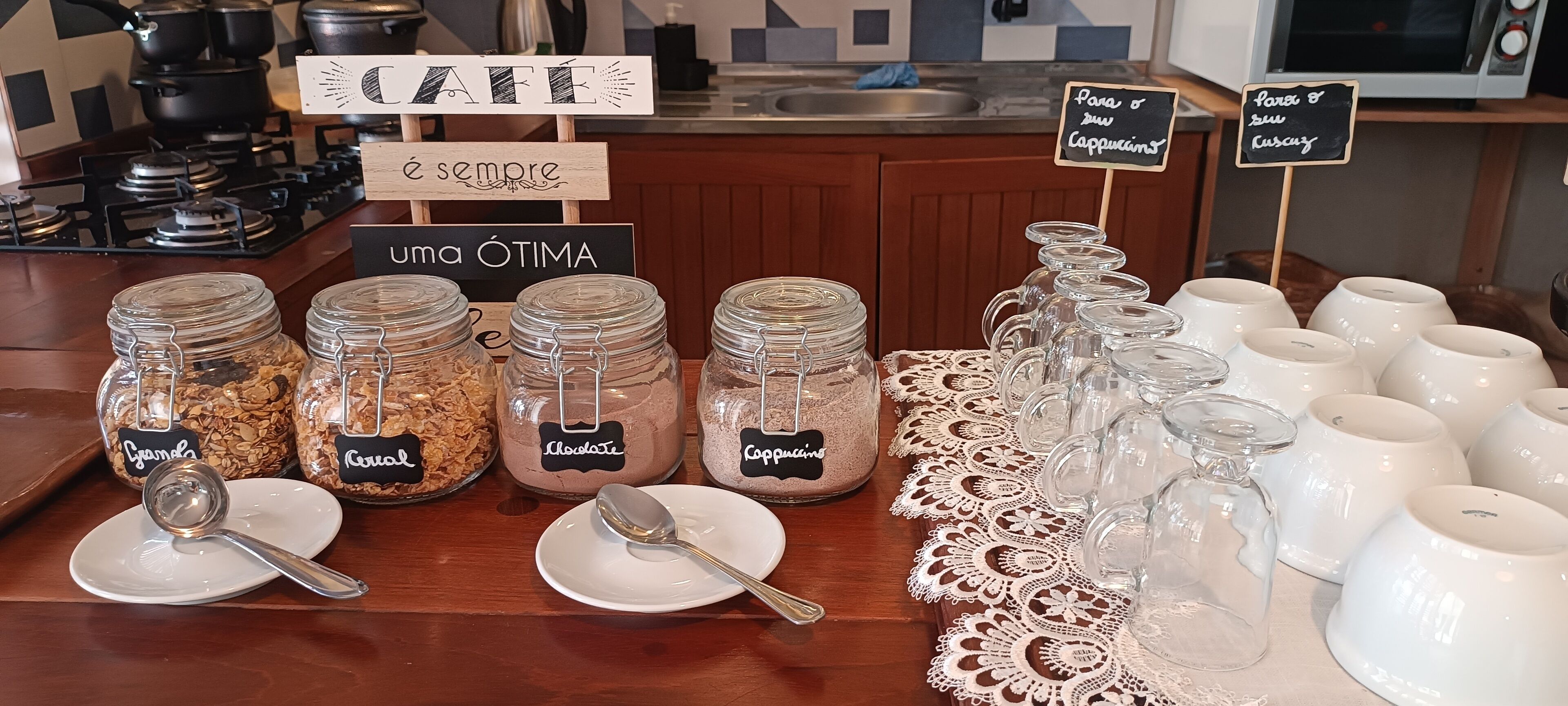 Un comptoir de petit-déjeuner avec des bocaux étiquetés contenant du granola, des céréales et du café, ainsi que des tasses et des assiettes en céramique blanche.