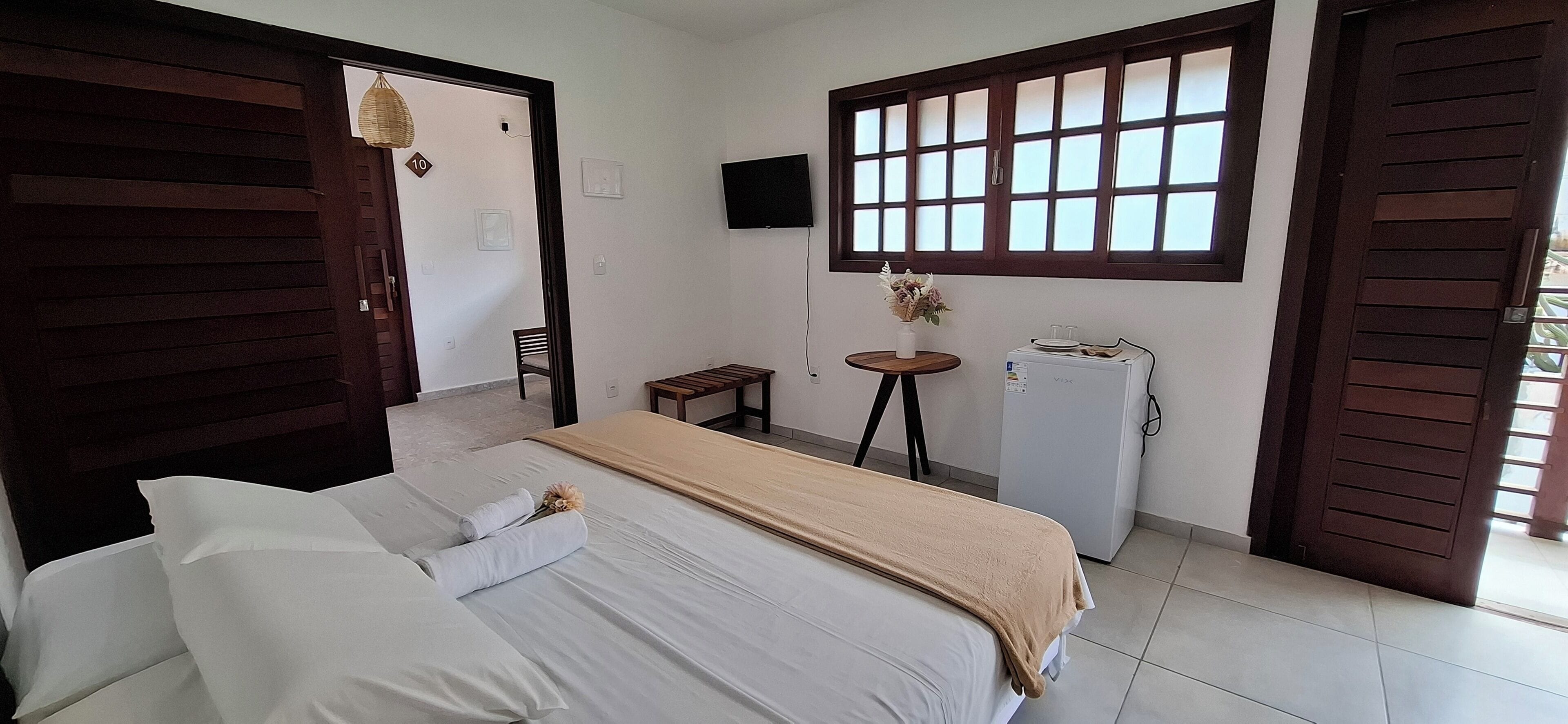A hotel room with a bed, a small table, a refrigerator, and a window with blinds.