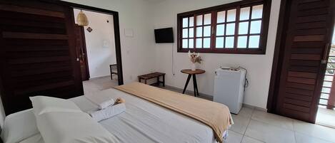A hotel room with a bed, a small table, a refrigerator, and a window with blinds.