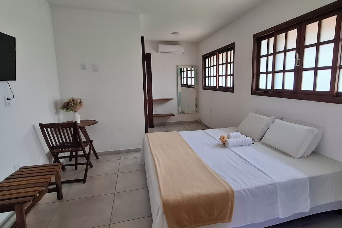 A hotel room with a bed, a desk, a chair, a TV, and a window with a view.