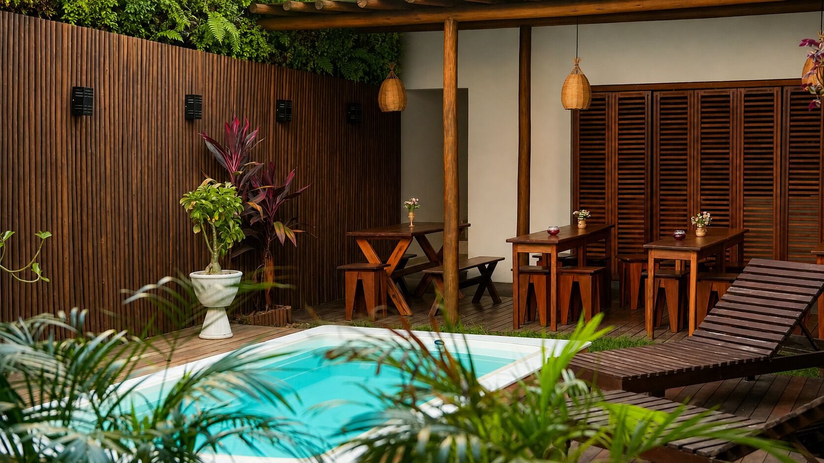 A wooden deck with a pool, surrounded by lush greenery and wooden furniture.