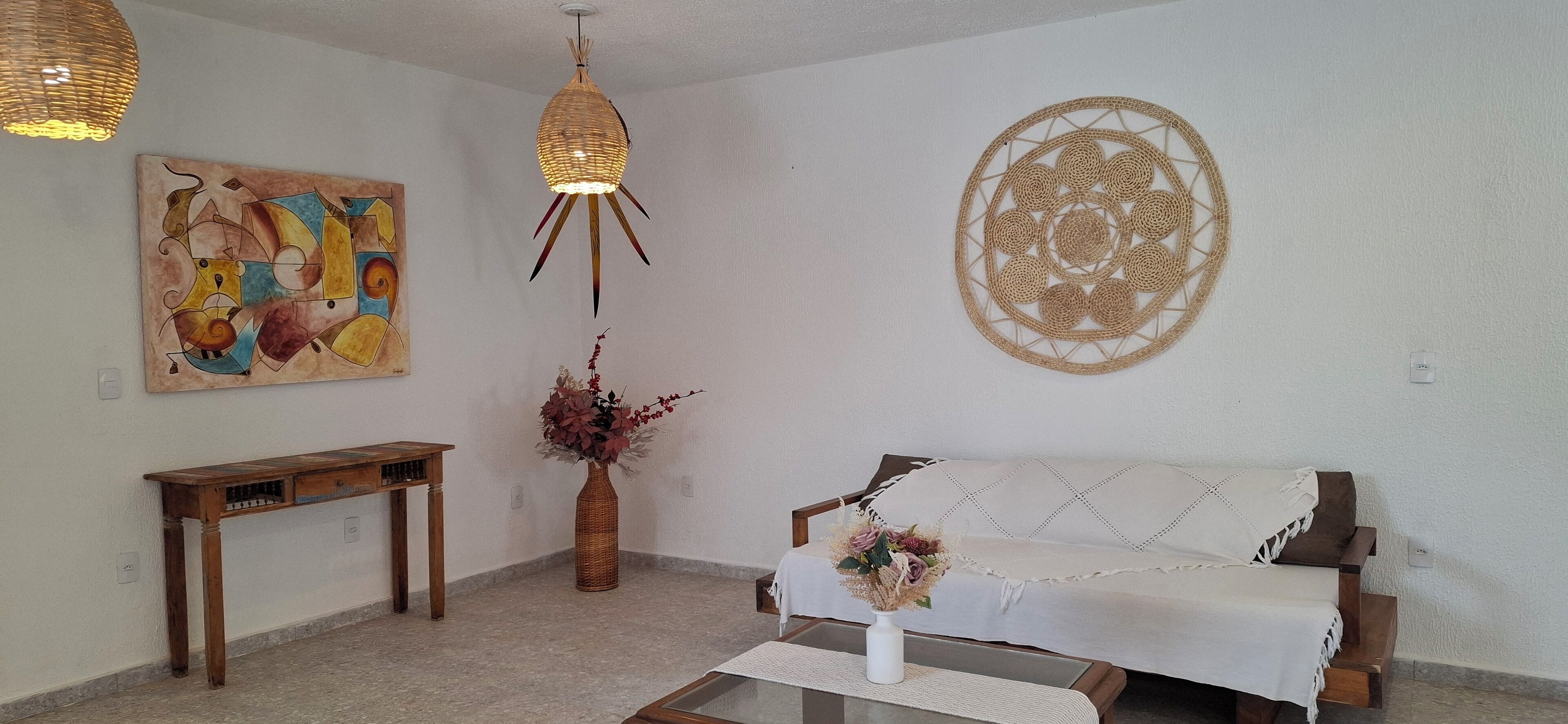 A living room with a wooden bench, a white sofa, a woven wall hanging, and a painting on the wall.