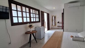 Una moderna camera d'albergo con un ampio letto, un tavolino con un vaso, un frigorifero e una TV a parete.
