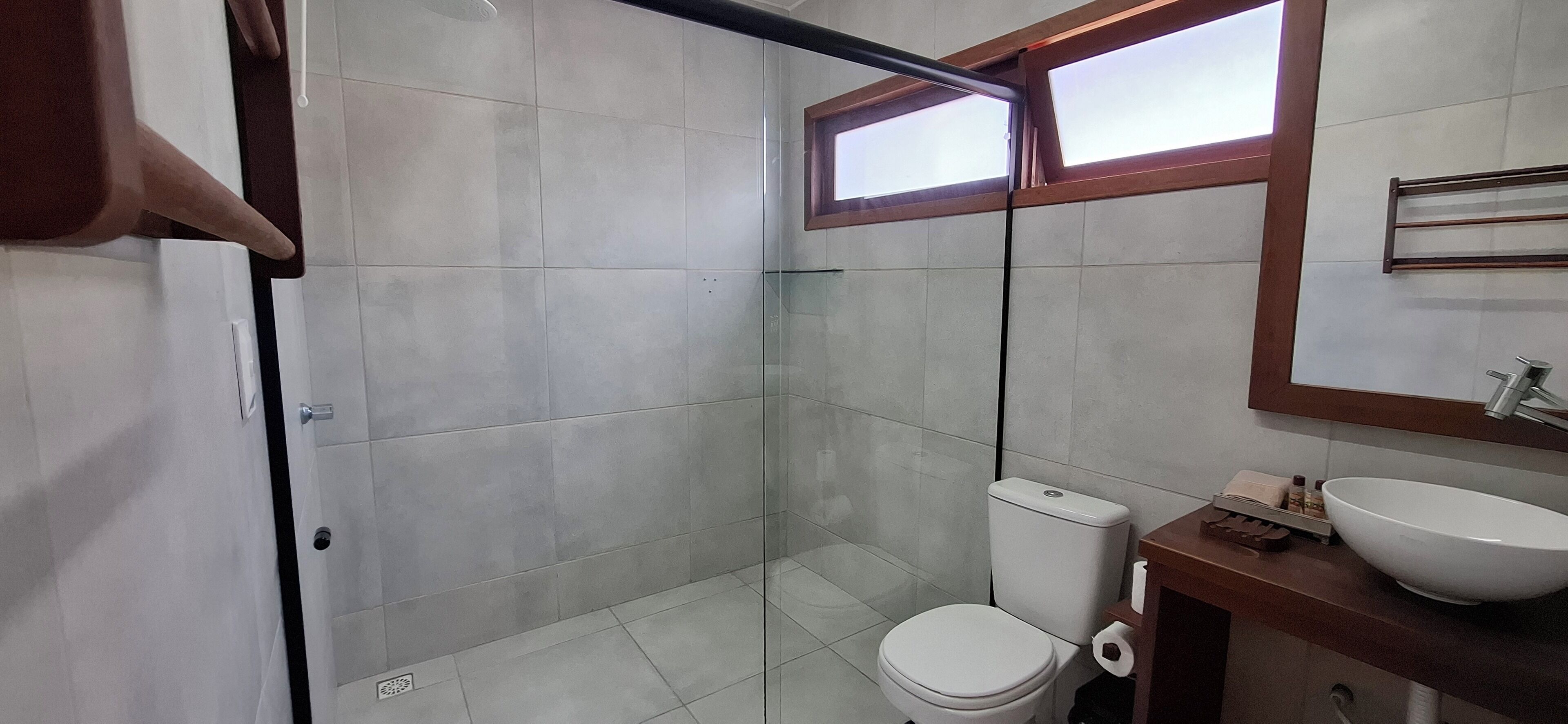 A modern bathroom with a glass shower enclosure, a white toilet, and a wooden vanity with a large sink.