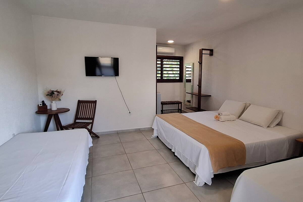 A hotel room with two single beds, a desk, a chair, a TV, and a window with blinds.