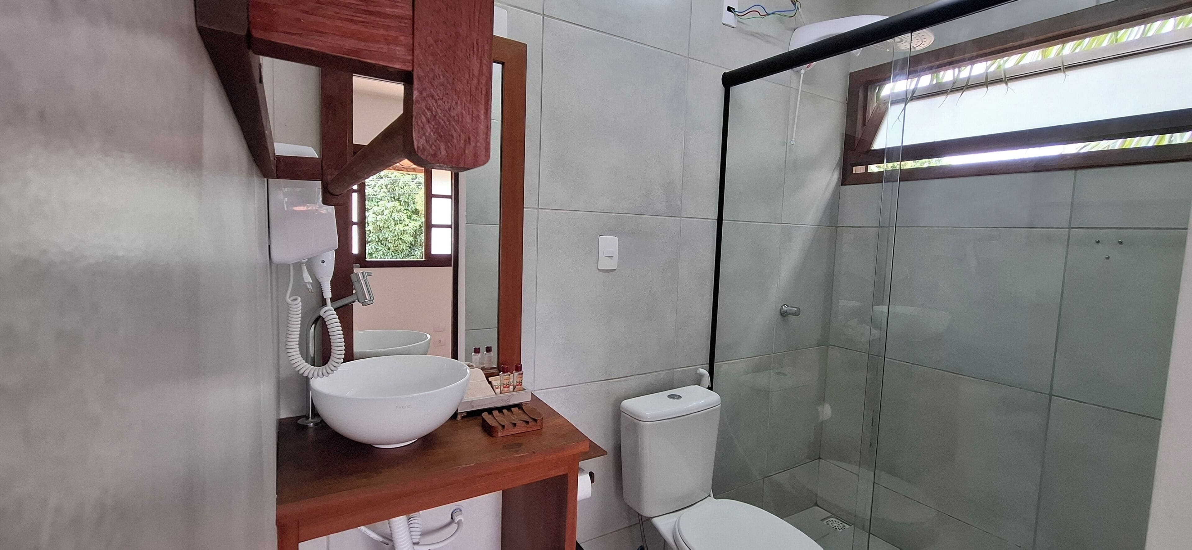 Une salle de bain avec un meuble-lavabo en bois, un lavabo blanc, des toilettes et une cabine de douche en verre.