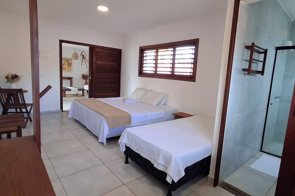 A room with two beds, a wooden table, and a shower area.