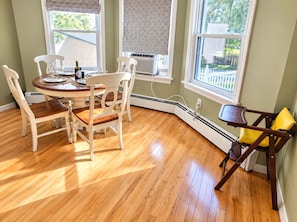A dining area with a round table, four chairs, and a window with a view of a fence and trees.