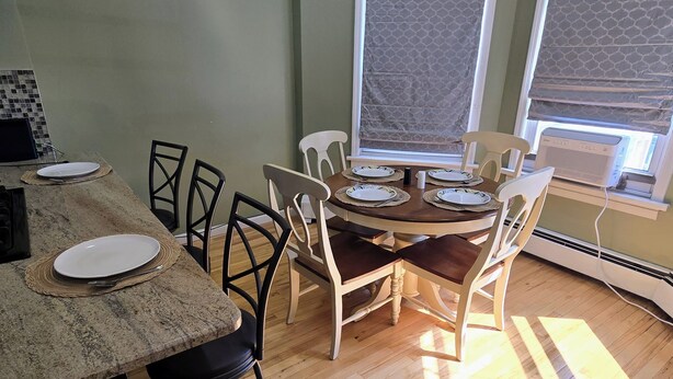 Un comedor con una mesa y sillas de madera, una encimera de cocina con un plato y cubiertos, y una ventana con una persiana estampada.