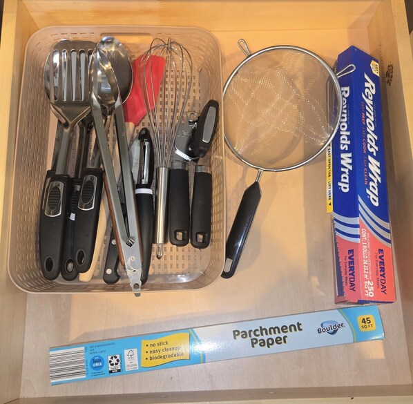 A drawer containing kitchen utensils, a strainer, and a box of Reynolds Wrap.