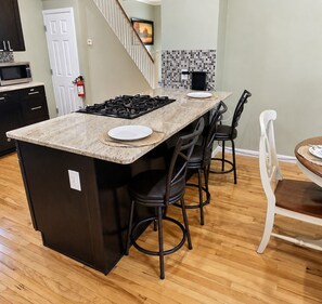 A kitchen with a central island, black chairs, a dining table with chairs, and a tiled backsplash.