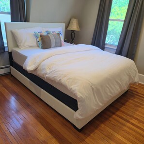 Una cama con ropa de cama blanca, un cabecero oscuro y una almohada estampada.
