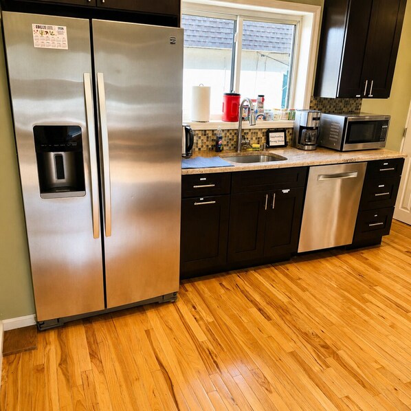 A kitchen with stainless steel appliances, a dishwasher, and a window with blinds.