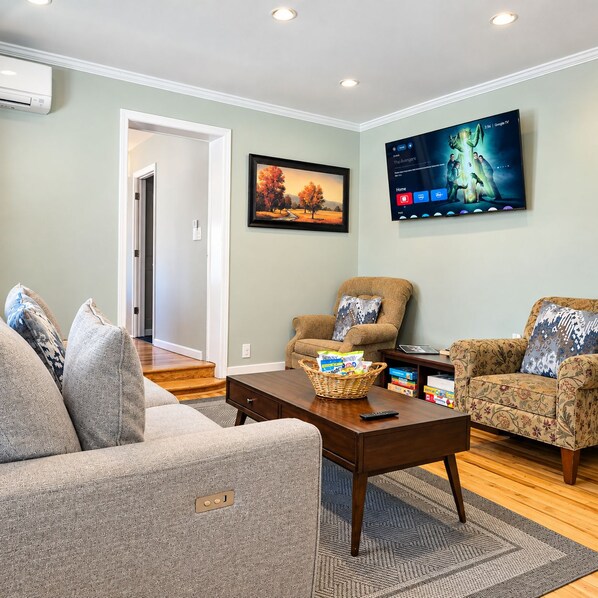 A living room with a sofa, armchairs, a coffee table, and a flat-screen TV mounted on the wall.