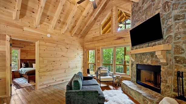 L’intérieur d’une cabane en rondins, avec une cheminée en pierre, un téléviseur fixé au mur et un coin salon confortable.