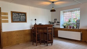 A room with a wooden table and chairs, a blackboard with chalk writing, a radiator, and a window with decorative items. - Hostal Lago Cóndor Patagonia (Puerto Natales)