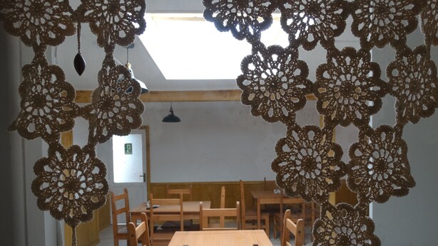 A dining area with a wooden table and chairs, a ceiling light, and a view of a room with a door and a window. - Hostal Lago Cóndor Patagonia (Puerto Natales)