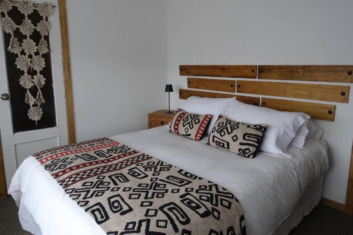 Una cama bien hecha con ropa de cama estampada, cabecera de madera y lámpara de noche.