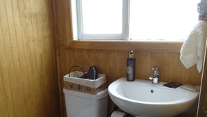 A compact bathroom with a white toilet, a pedestal sink, and a small trash bin. - Hostal Lago Cóndor Patagonia (Puerto Natales)