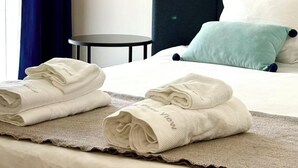 A neatly made bed with folded towels, a dark headboard, and a hanging pendant light. - Expo river View (Lisboa)