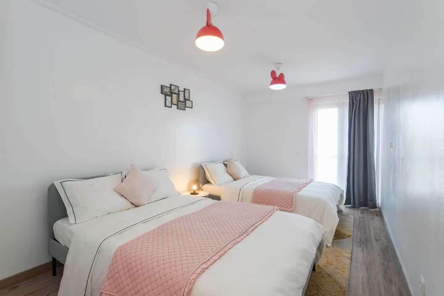 Een hotelkamer met twee bedden, een klein nachtkastje met een lamp, een wandklok en een raam met gordijnen.