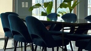 A modern dining area with a glass table, blue chairs, and a view of a cityscape through large windows. - Expo river View (Lisboa)