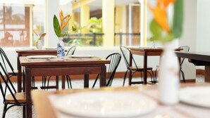 Un espace repas avec des tables et des chaises, un vase rempli de fleurs et une vue sur l’intérieur du bâtiment.