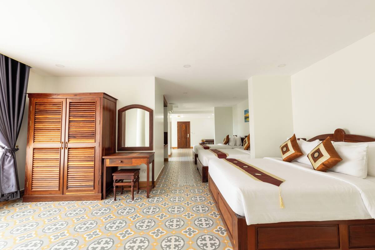 Une chambre d’hôtel dotée d’une grande armoire, d’un bureau, d’un lit avec plusieurs oreillers et d’un sol à motifs.