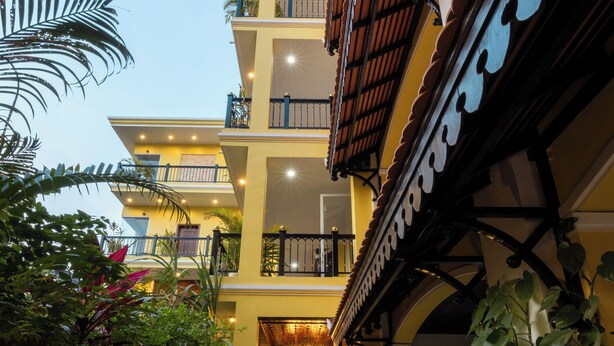 Un hotel de varios pisos con un patio central, balcones y plantas en macetas a lo largo del paseo.