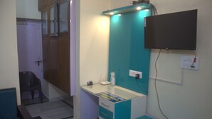 Quarto pequeno e compacto com escrivaninha, cadeira e televisão fixada na parede.