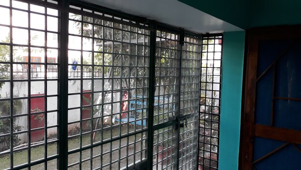 Visão através de um portão de metal com uma porta azul, dando para uma área externa com plantas em vasos e uma estrutura vermelha.