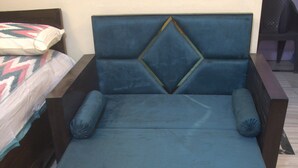 Uma cama de solteiro com cabeceira e peseira azuis, duas almofadas e estrutura de madeira.