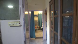 Corredor estreito que dá para um quarto com cama, janela e cortina.