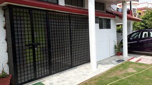 Uma entrada fechada por portão de metal, um vaso de planta e um carro estacionado.