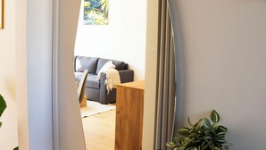 A modern living room with a large mirror, a grey sofa, a wooden coffee table, and a potted plant. - Stylish Central 4-person CPH Apt. (København)