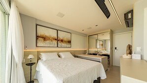 A modern hotel room with a large bed, bedside table, and a desk with a chair. There is a large mirror above the desk and artwork on the wall. - RSR - Modern Studios on the Edge of Maceio (Maceió)