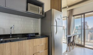 A modern kitchen with a stainless steel refrigerator, wooden cabinets, and a black countertop. - Studio in Condominium With Pool in Paraiso Onp1716 (São Paulo)