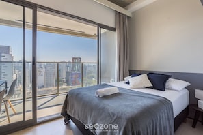 A modern bedroom with a large bed, a view of the city through floor-to-ceiling windows, and a balcony with a chair. - Studio in Condominium With Pool in Paraiso Onp1716 (São Paulo)