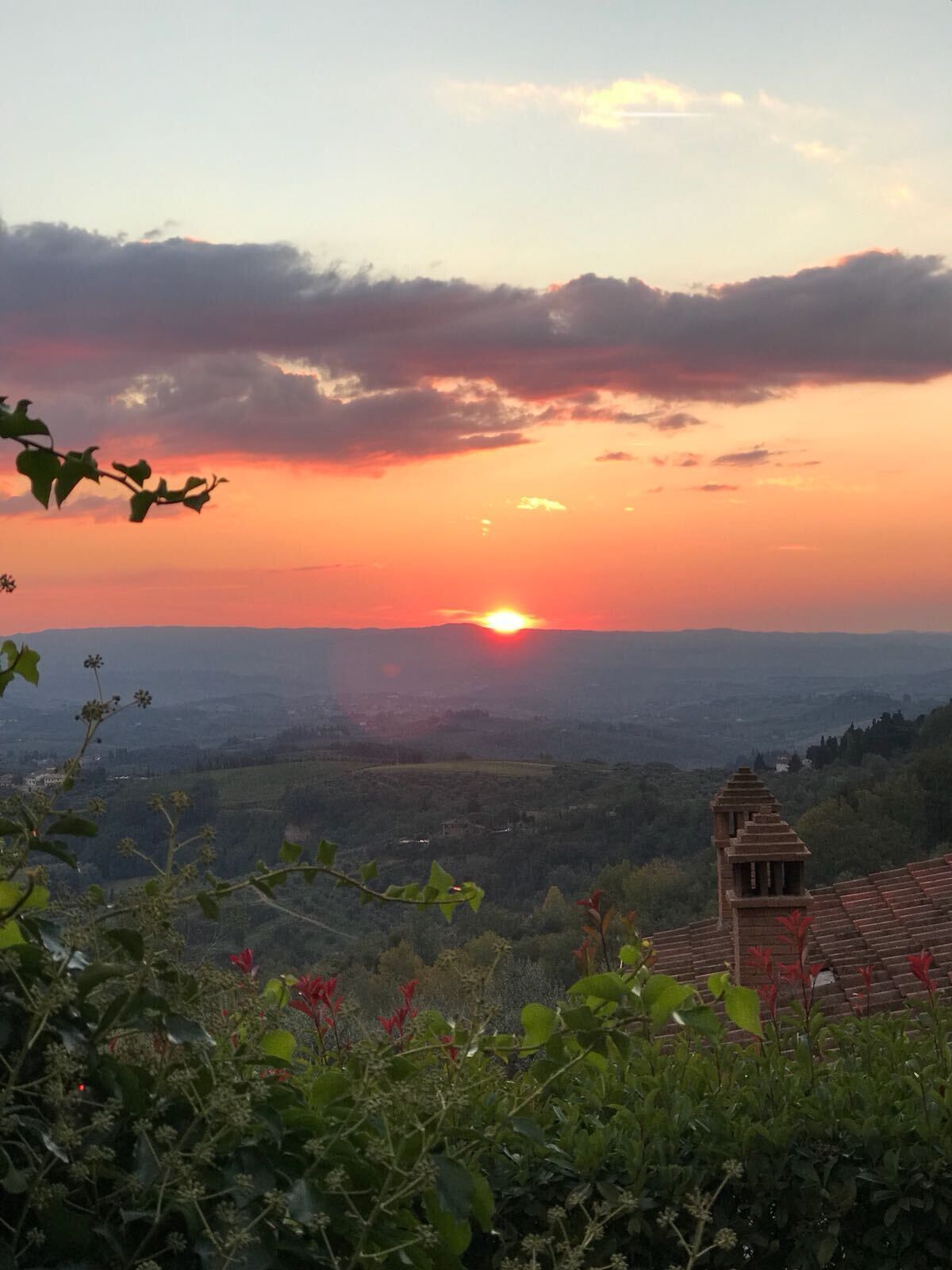 Une vue sur le coucher de soleil depuis un point de vue élevé, dominant une vallée où se trouve un bâtiment traditionnel avec un toit en tuiles.