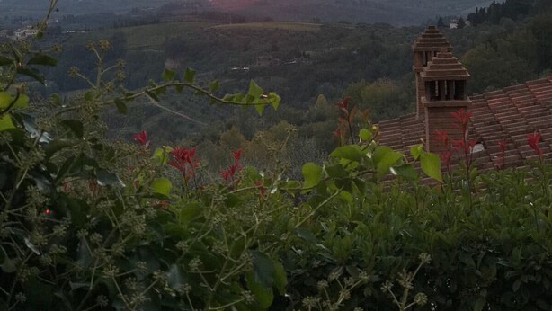 Sonnenuntergangsblick von einer erhöhten Aussichtslage über ein Tal mit einem traditionellen Gebäude mit Ziegeldach.