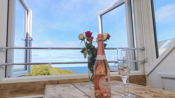 A bottle of Conte Paladio Prosecco rosé and a glass on a wooden table by a window with a view of the sea. - Seagulls Nest (St Ives)